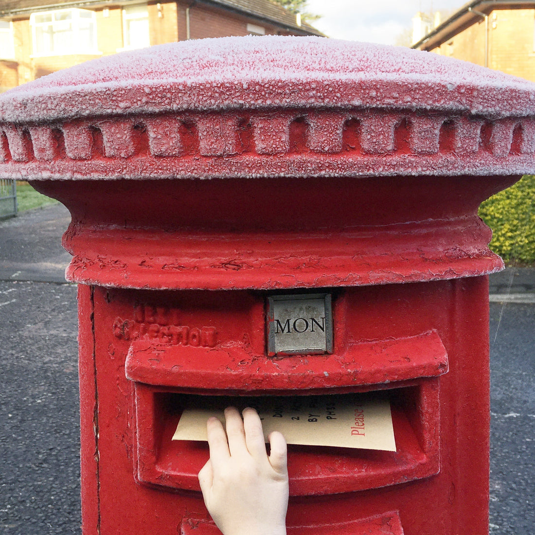 Red postbox covered in frost with child's hand posting a Christmas card