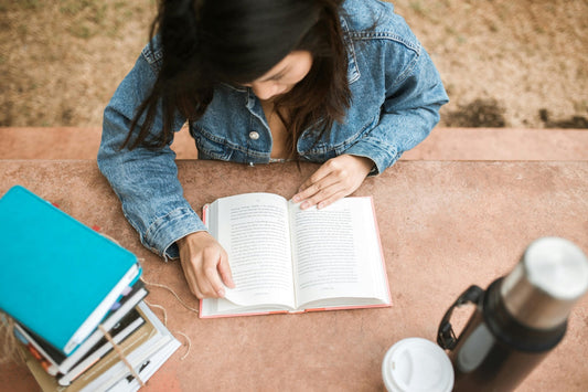 woman reading outside with a flask of coffee and a stack of books