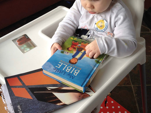 toddler reading children's my little bible in highchair