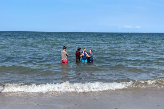 four people participate in an adult baptism in the sea 