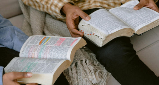 Two people sitting side by side hold their bibles open to read