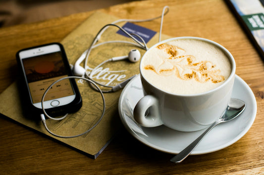 image from unspash showing a phone listening to a podcast on headphones with a cup of coffee on a table