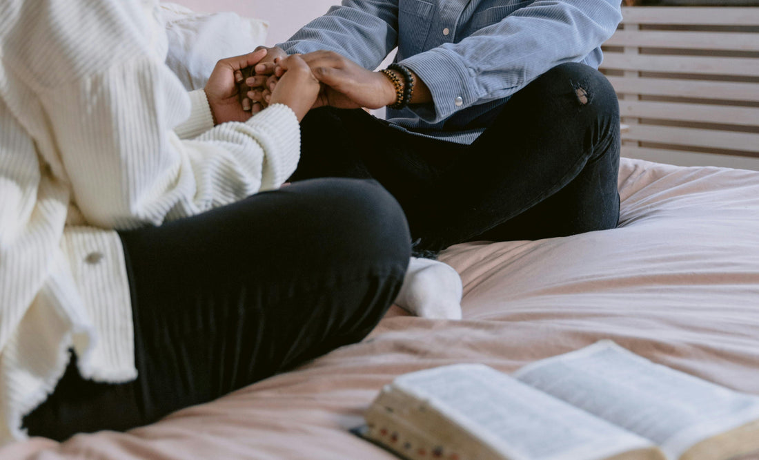 Two people sitting crossed leg on a bed with bible open beside them cultivating a prayer habit together
