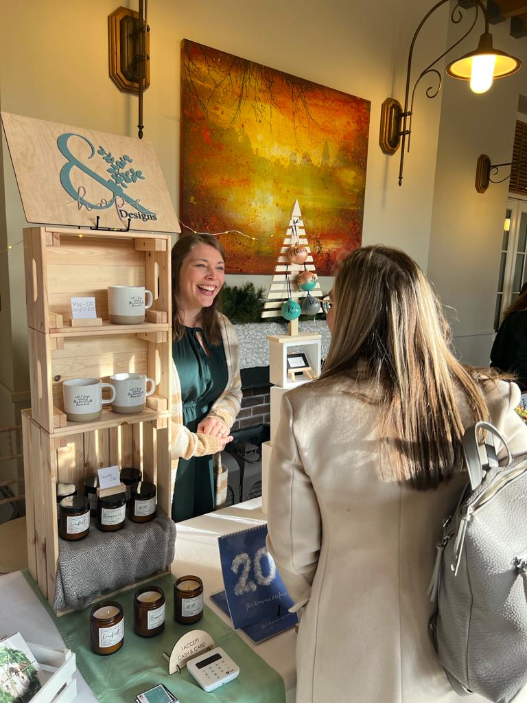 Anna interacts with a customer at the Cohen and co market in montalto estate, surrounded by and Hope designs products on her stall